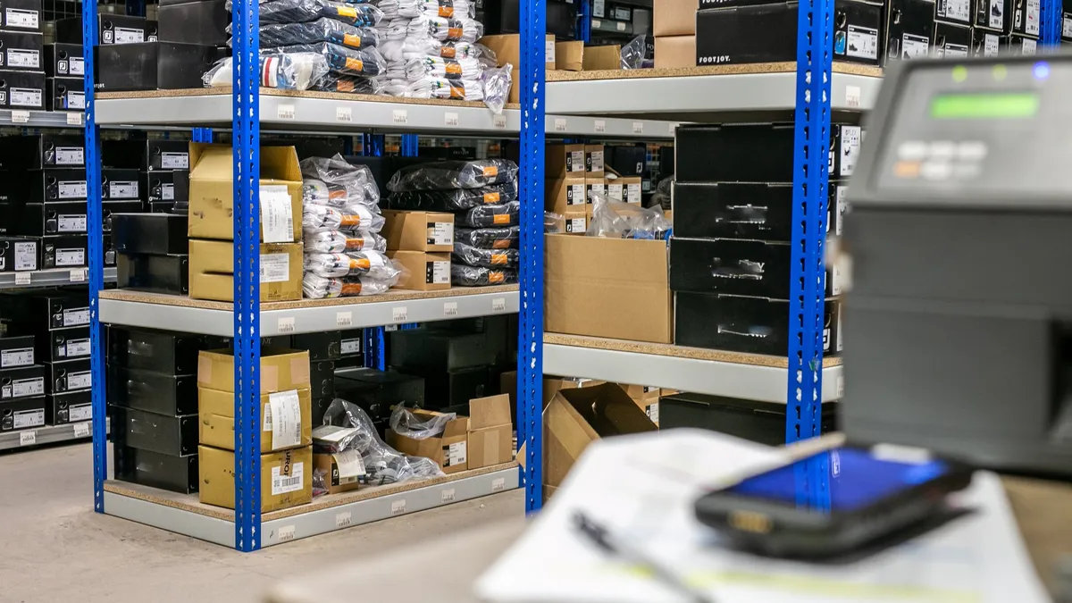 A dispatch area with picking shelves, cartons and poly-bagged stock beside a label printer and handheld scanner on the packing bench