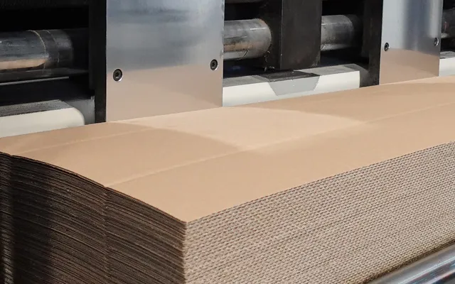 A stack of plain unprinted kraft corrugated blanks in front of the print and slotting units of a converting line