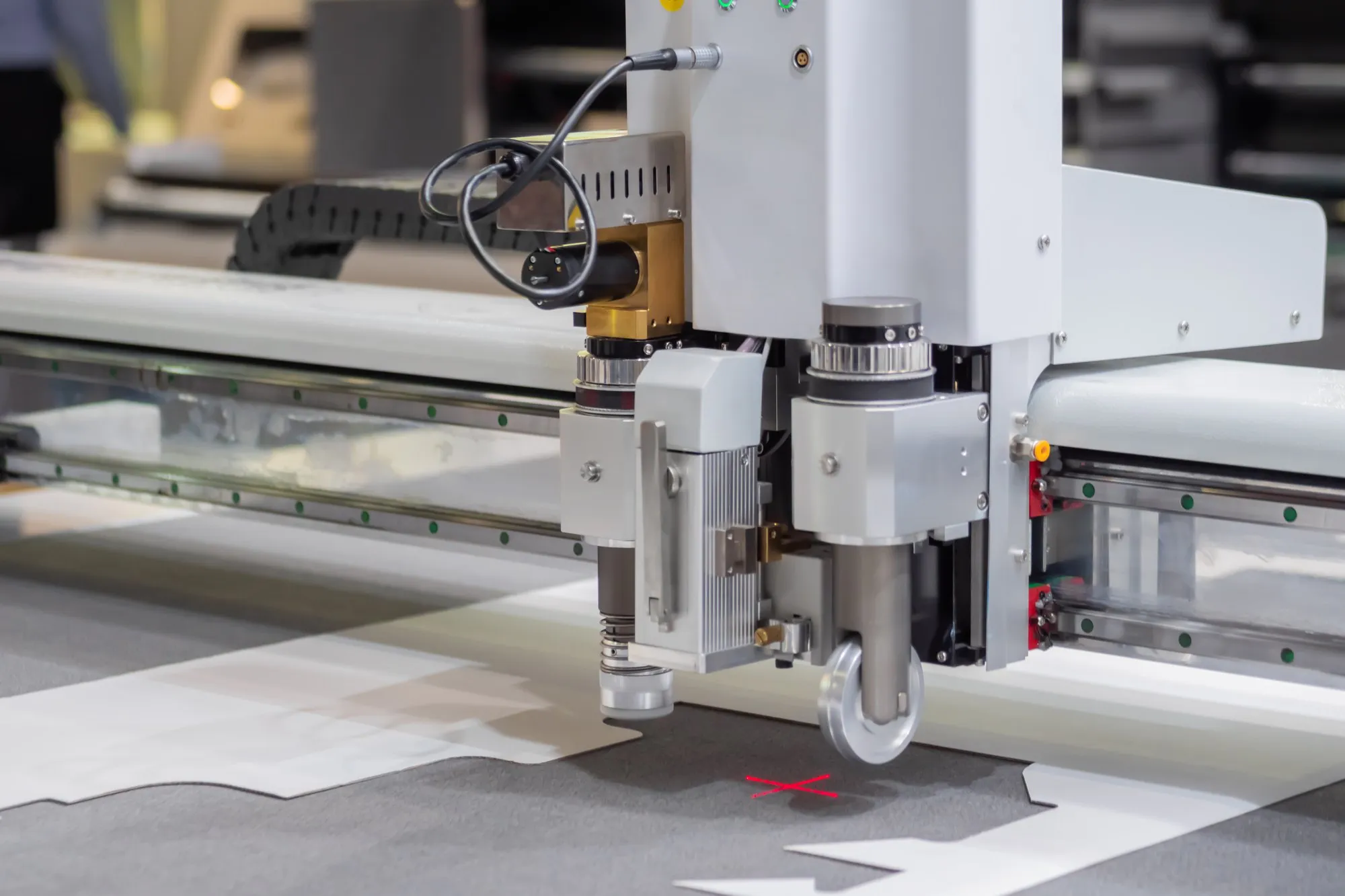 A digital flatbed cutting table cutting a sample, with the knife and creasing wheel head travelling across the bed