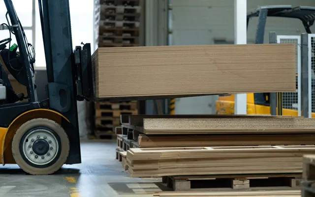 A forklift moving a stack of corrugated board sheets across a production floor