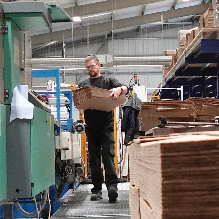 A Tradepack operator carrying a stack of die-cut corrugated blanks through the production hall
