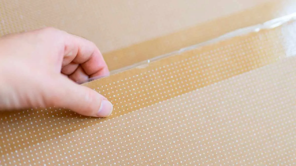 A hand peeling the release liner from a peel and seal strip on a corrugated mailer