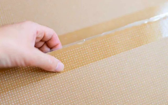 A hand peeling the release liner from a peel and seal strip on a corrugated mailer