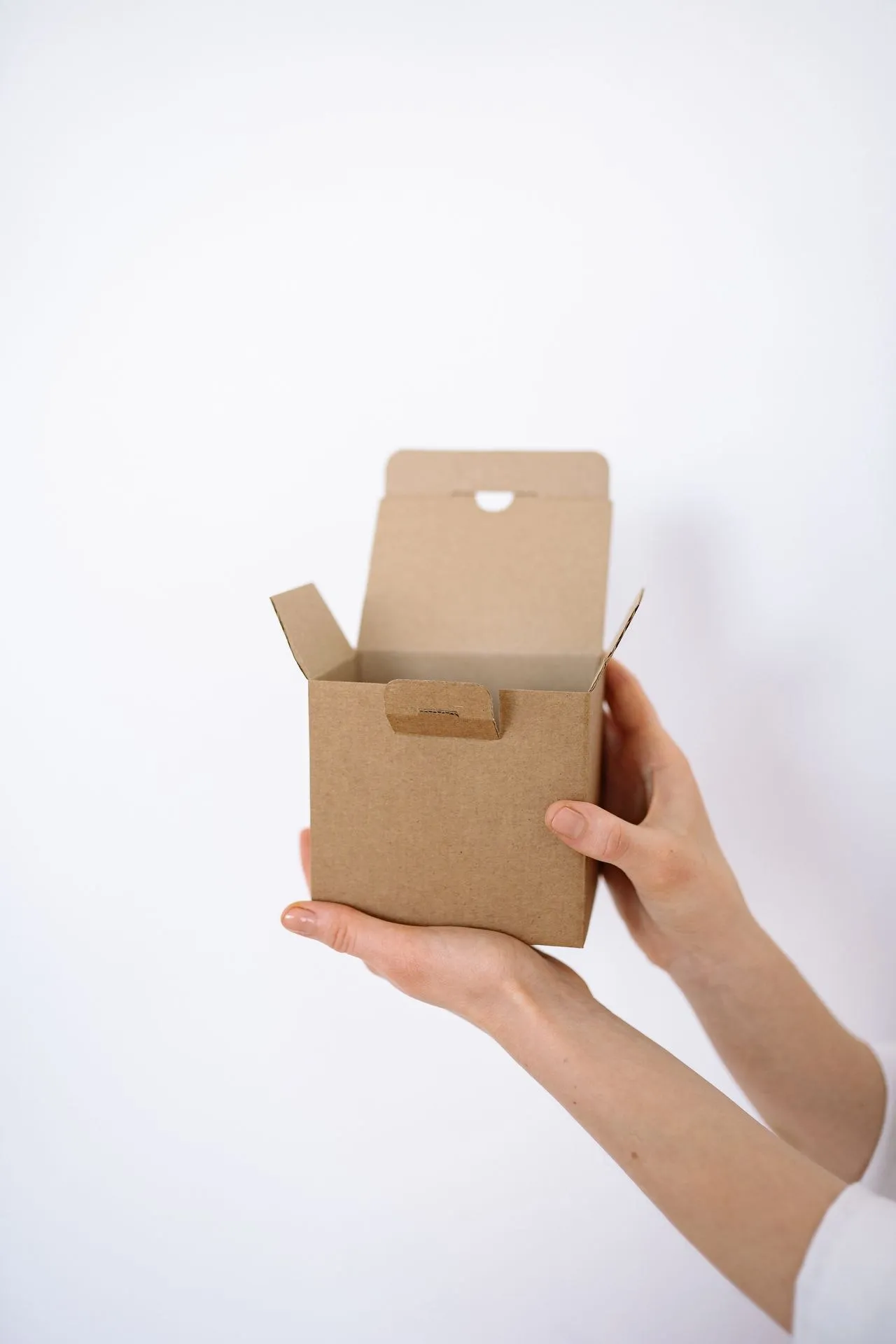 A small die-cut corrugated box with a tuck-top lid, held in both hands