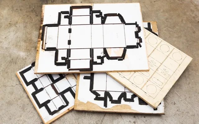 Flat steel rule cutting formes stacked on a factory floor, with the knives set into plywood