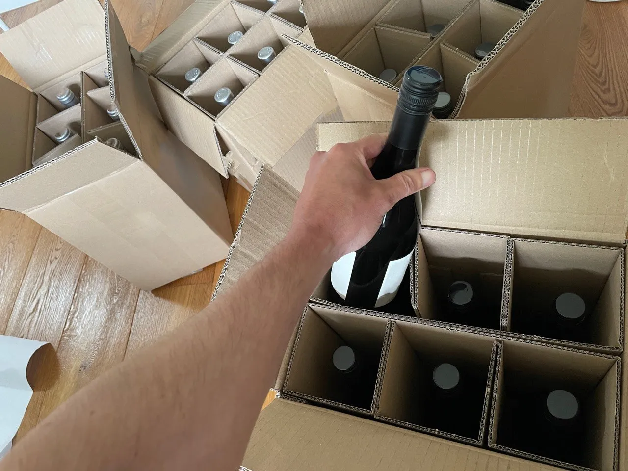 A bottle being lowered into the full-height cells of a corrugated wine divider