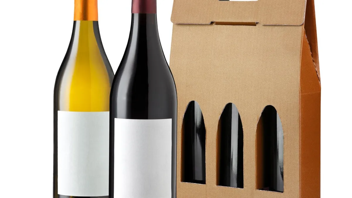 A three-bottle corrugated gift carrier with die-cut windows and a hand hole, beside two unlabelled wine bottles